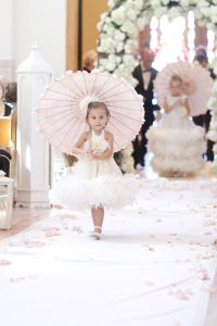 young girl walking down aisle at wedding carrying parasol